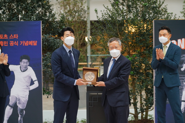 조폐공사 반장식 사장이 손 선수에게 손흥민 기념메달 동판을 증정하고 있다.(사진설명 : 왼쪽 손흥민 선수, 오른쪽 조폐공사 반장식 사장, 축하해 주는 현대백화점 정지영 부사장)